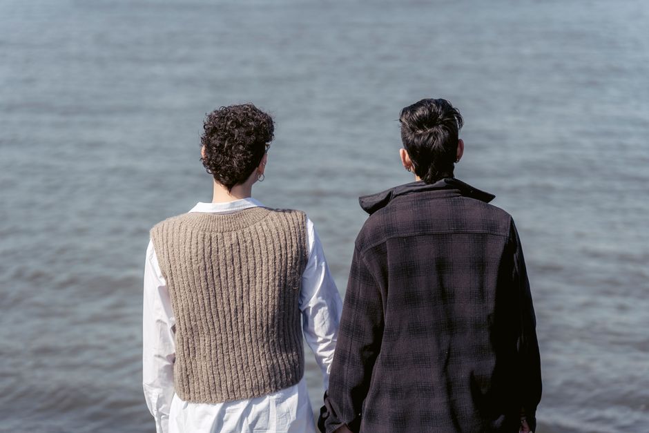 Back view of unrecognizable best friends in warm clothes admiring rippling water of river