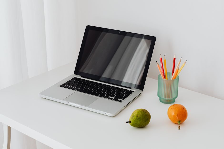 A clean and modern workspace featuring a laptop, colorful pencils, and fresh fruits on a white desk.