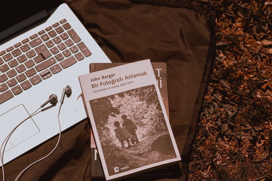 From above of computer with earphones near books placed on cloth during picnic