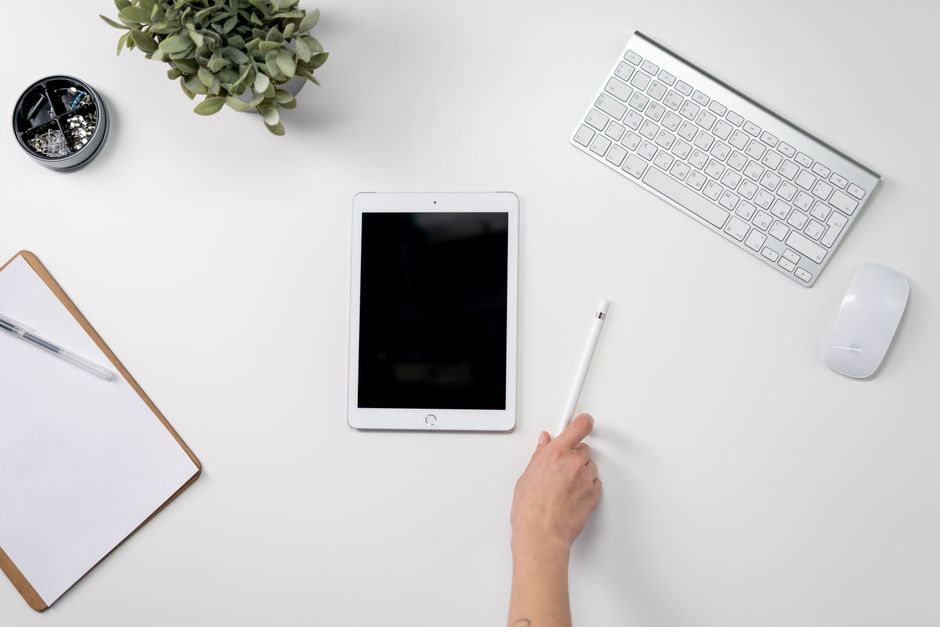 A clean and organized home office setup featuring a tablet, stylus, keyboard, and potted plant.