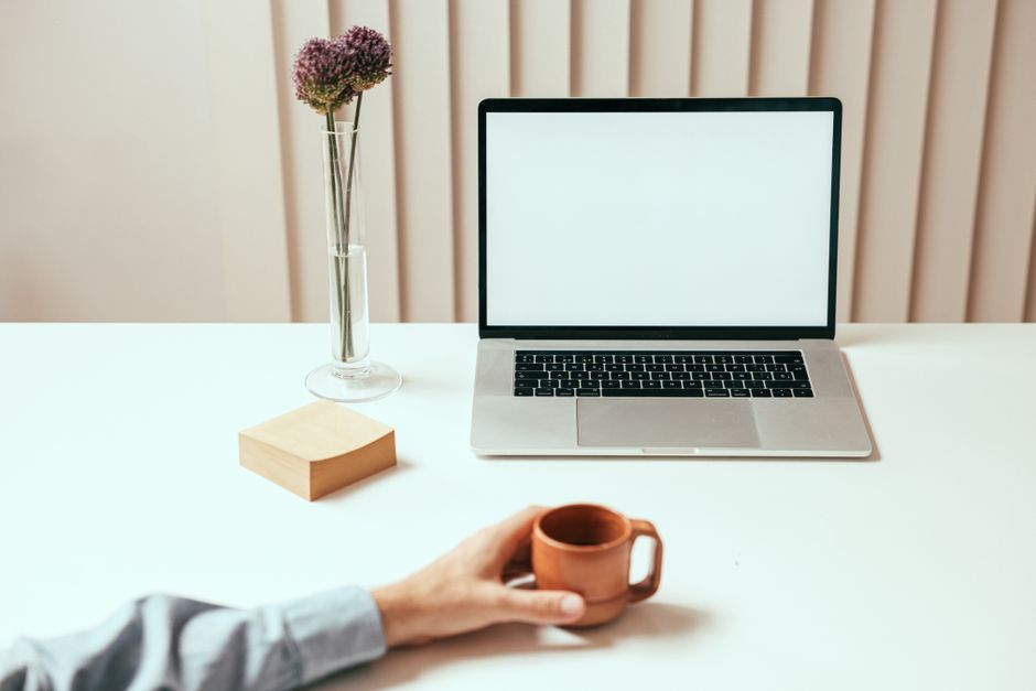 A minimalist workspace setup featuring a laptop, coffee mug, and decorative vase with flowers.